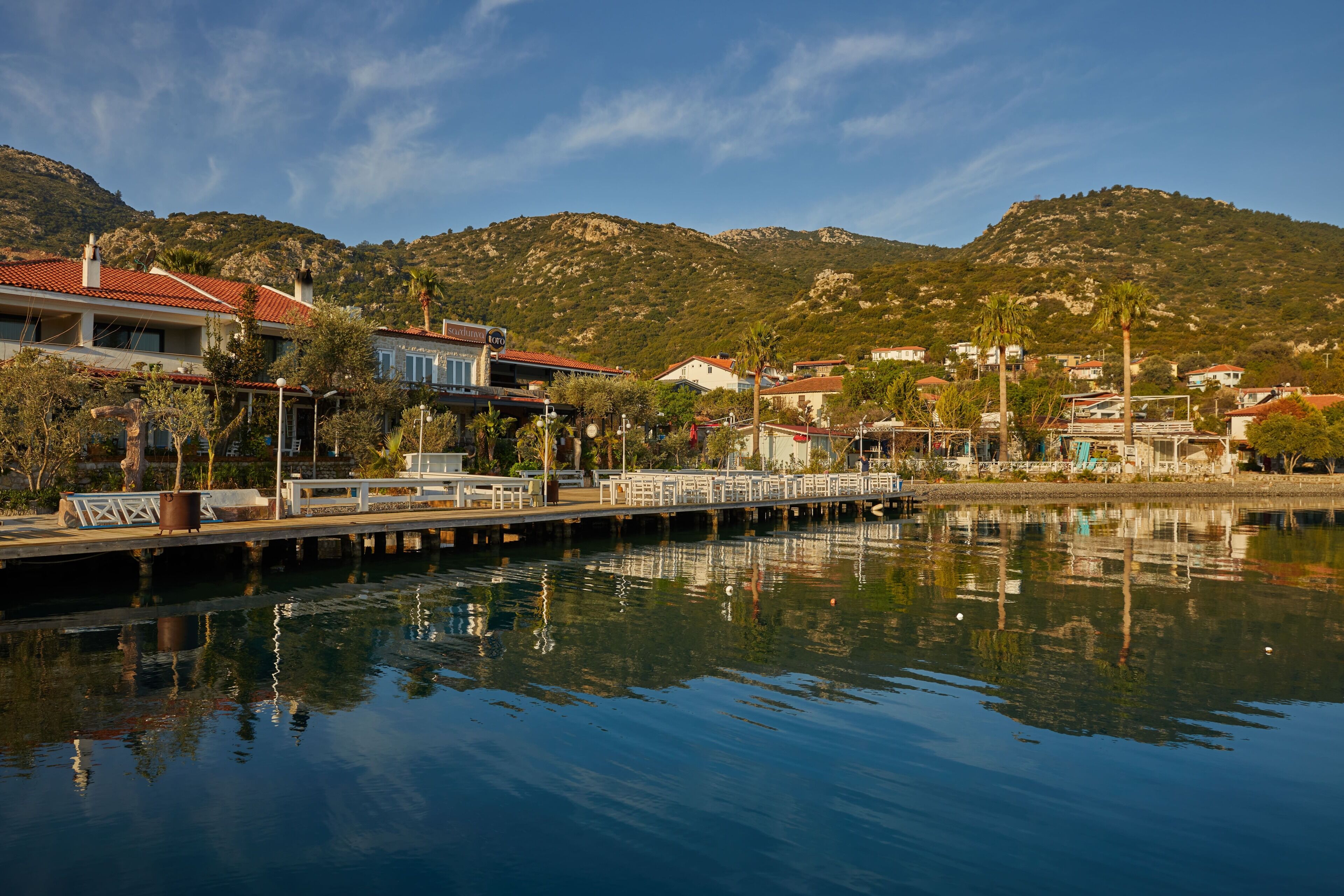 A waterfront property with a dock, buildings with red roofs, and a mountainous backdrop.