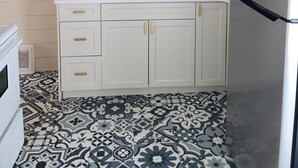Eine Küche mit weißen Schränken, einer schwarzen Küchenrückwand mit Fliesen, einem Edelstahl-Kühlschrank und einem Bodenbelag mit Musterfliesen.