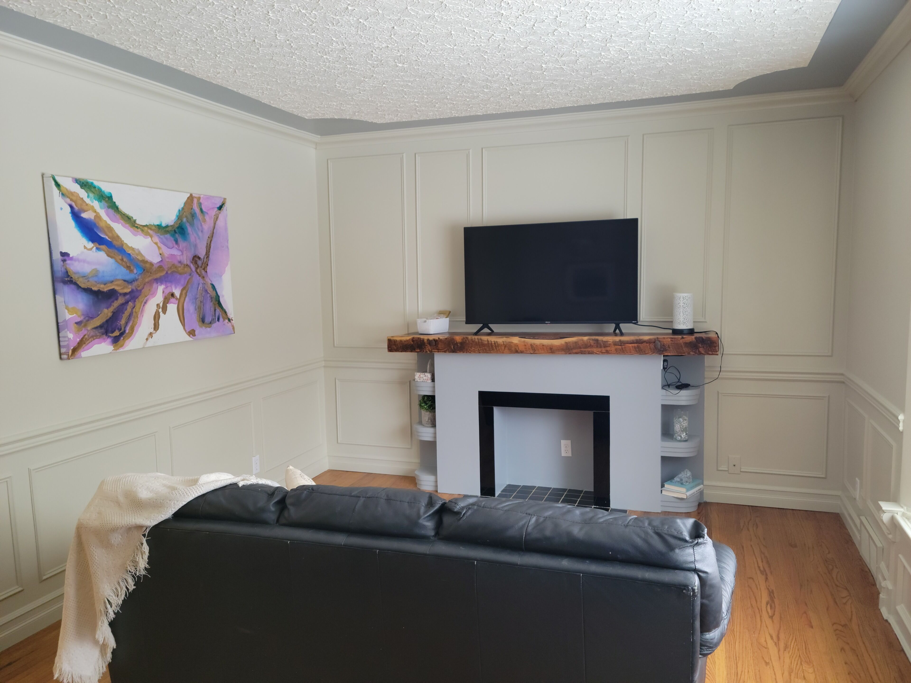 Un salon doté d’une cheminée, d’un téléviseur à écran plat fixé au-dessus et d’un tableau abstrait aux couleurs vives accroché au mur.