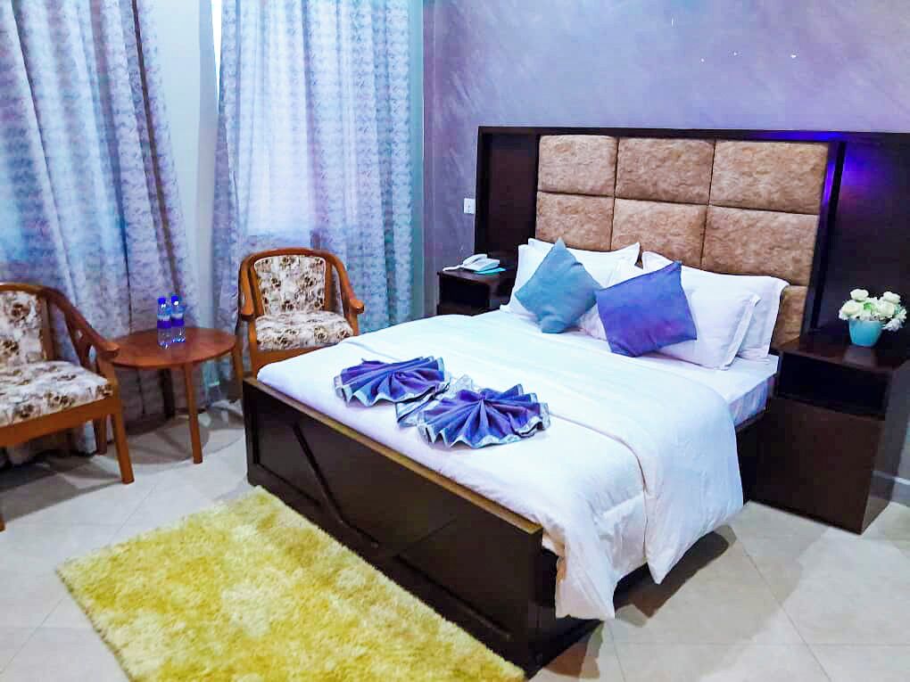 Une chambre à coucher avec un lit, deux chaises, une petite table, une table de chevet et une lampe de chevet.