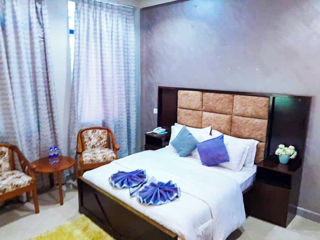 Una habitación de hotel con una cama, dos mesitas de noche, una silla, una pequeña mesa y cortinas.