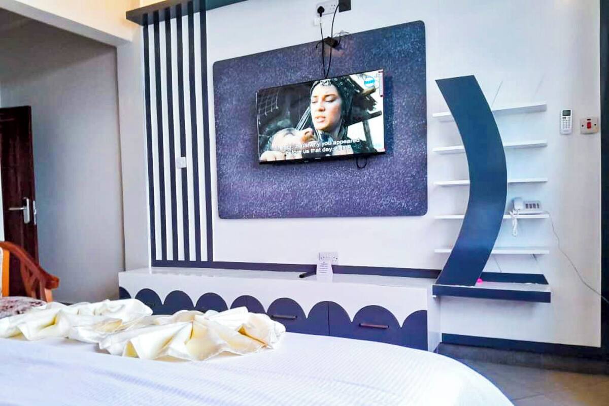 A modern hotel room with a large bed, a flat-screen TV mounted on the wall, and a built-in shelving unit.