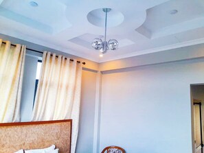 A hotel room with a bed, a chandelier, and a window with curtains. - RIVANA HOTEL GOBA (Dar es Salaam)