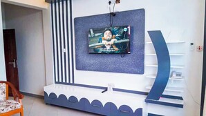 A modern living room with a flat-screen TV mounted on a wall, a built-in bench with storage, and a door leading to another room. - RIVANA HOTEL GOBA (Dar es Salaam)