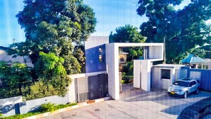 A modern building with a paved driveway, a car parked in front, and surrounding greenery. - RIVANA HOTEL GOBA (Dar es Salaam)