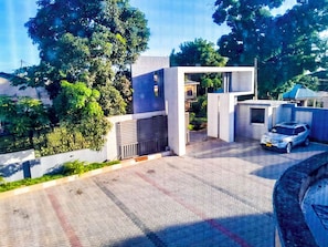 Un bâtiment moderne avec une allée pavée, une voiture garée devant et de la verdure tout autour.