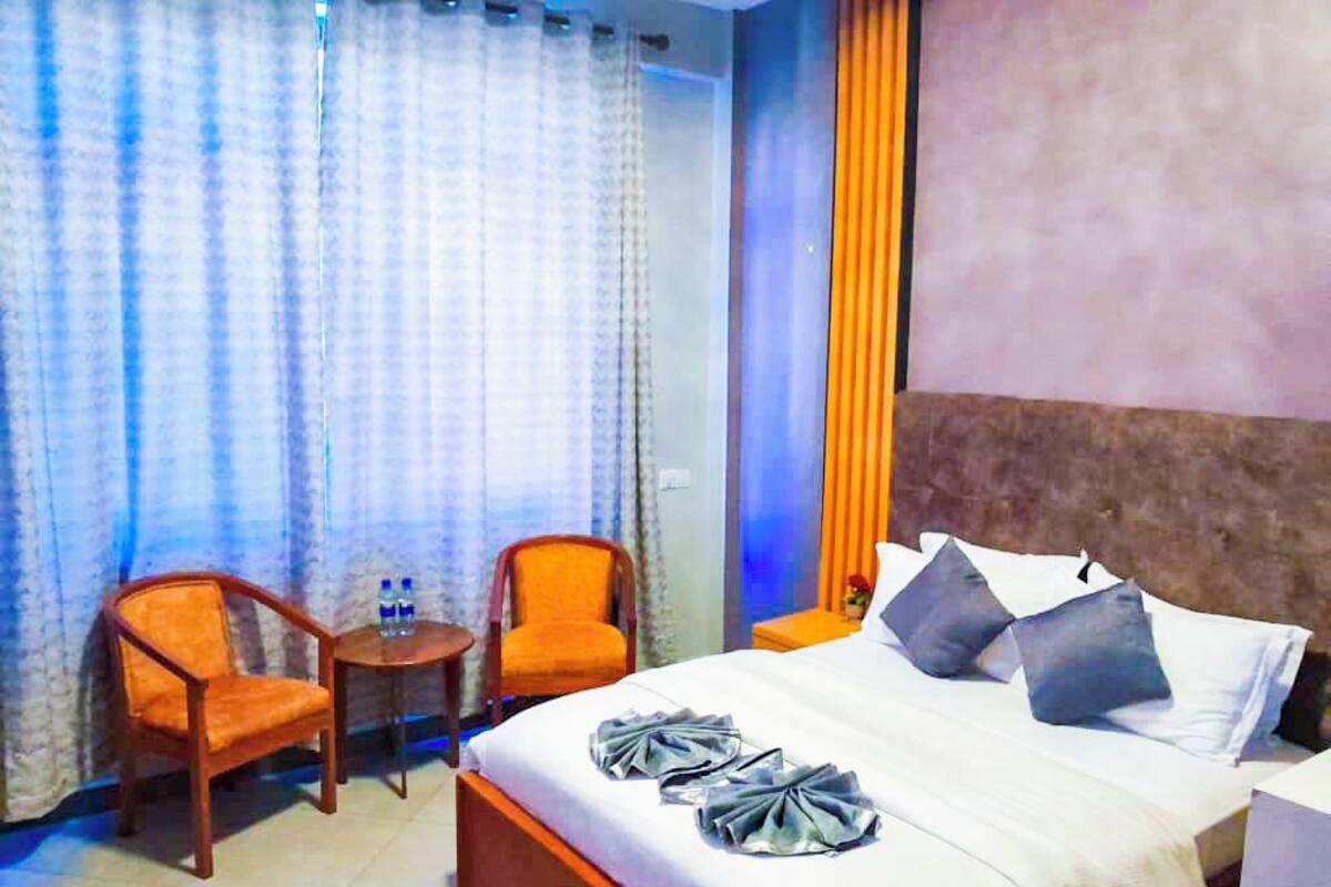 A hotel room with a bed, two chairs, a small table with water bottles, and a nightstand.
