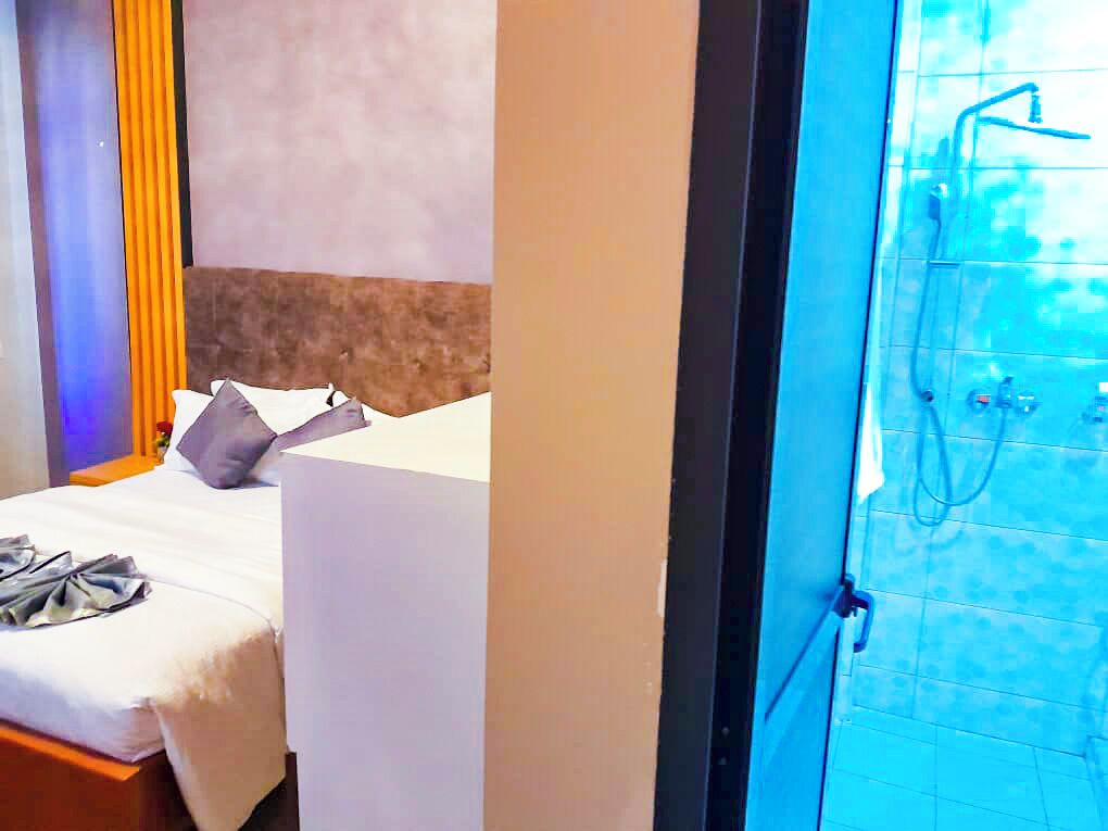Una habitación de hotel con cama, mesita de noche y baño con ducha.