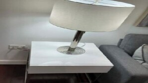 A modern lamp on a white bedside table in a room with a grey sofa.
