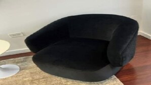 A black armchair in a room with a white wall and a wooden floor.