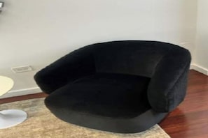 A black armchair in a room with a white wall and a wooden floor. - High-Floor 1BR Condo with Stunning NYC Skyline Views with AC  Prime Location (New York)
