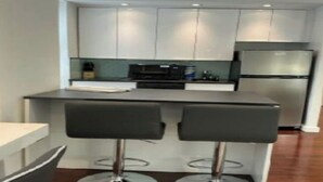 A modern kitchen with white cabinets, a stainless steel refrigerator, and a central island with two bar stools.