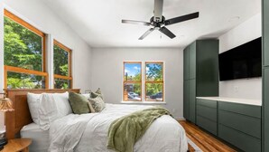 A bedroom with a bed, a ceiling fan, a TV, and a window with a view of trees. - Steps to Downtown The North End Gem (Boise)