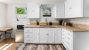 A kitchen with white cabinets, a granite countertop, a built-in microwave, a sink, and a window with a view of greenery. - Steps to Downtown The North End Gem (Boise)