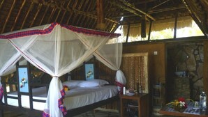 Una habitación con una cama bajo una mosquitera, suelo de piedra, una mesa de madera con un florero y una pared de piedra.