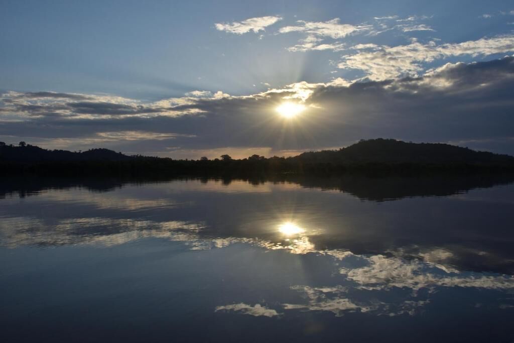 A calm lake with the sun reflecting on the water, surrounded by hills.