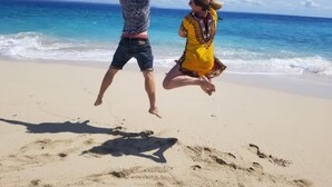 Dos personas saltando en una playa arenosa con el océano al fondo.