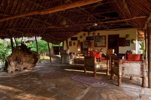 A rustic thatched-roof structure with stone flooring, wicker furniture, and a large tree trunk.