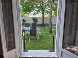A view through a window of a backyard with a lawn, two chairs, and a table. - T2 apartment for rent 7Km from the ocean (Notre-Dame-de-Riez)