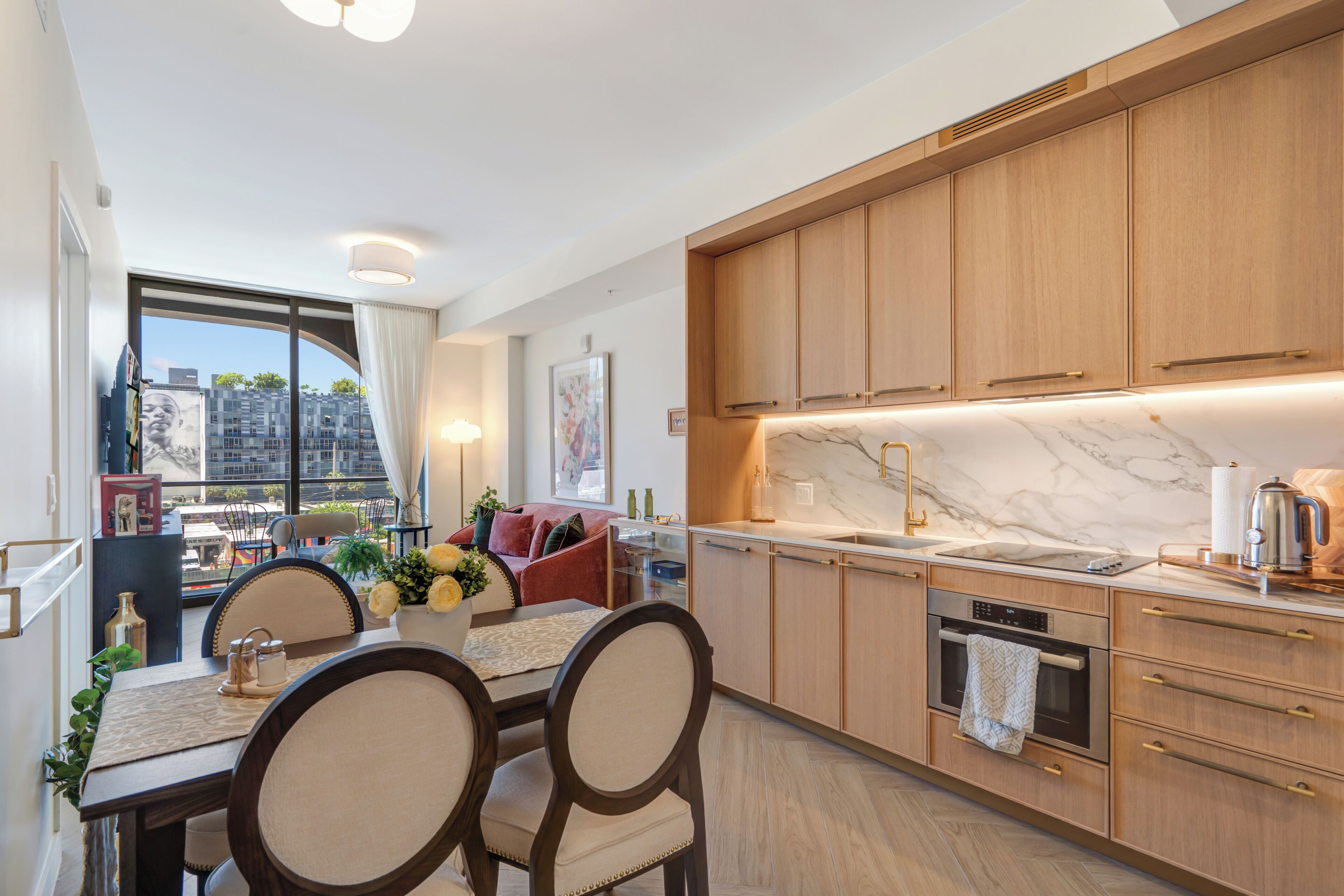 A modern kitchen with wooden cabinets, a marble countertop, and a dining area with a table and chairs.