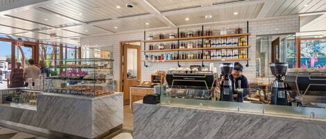 A modern cafe with marble countertops, a coffee bar, and shelves with jars and bottles.