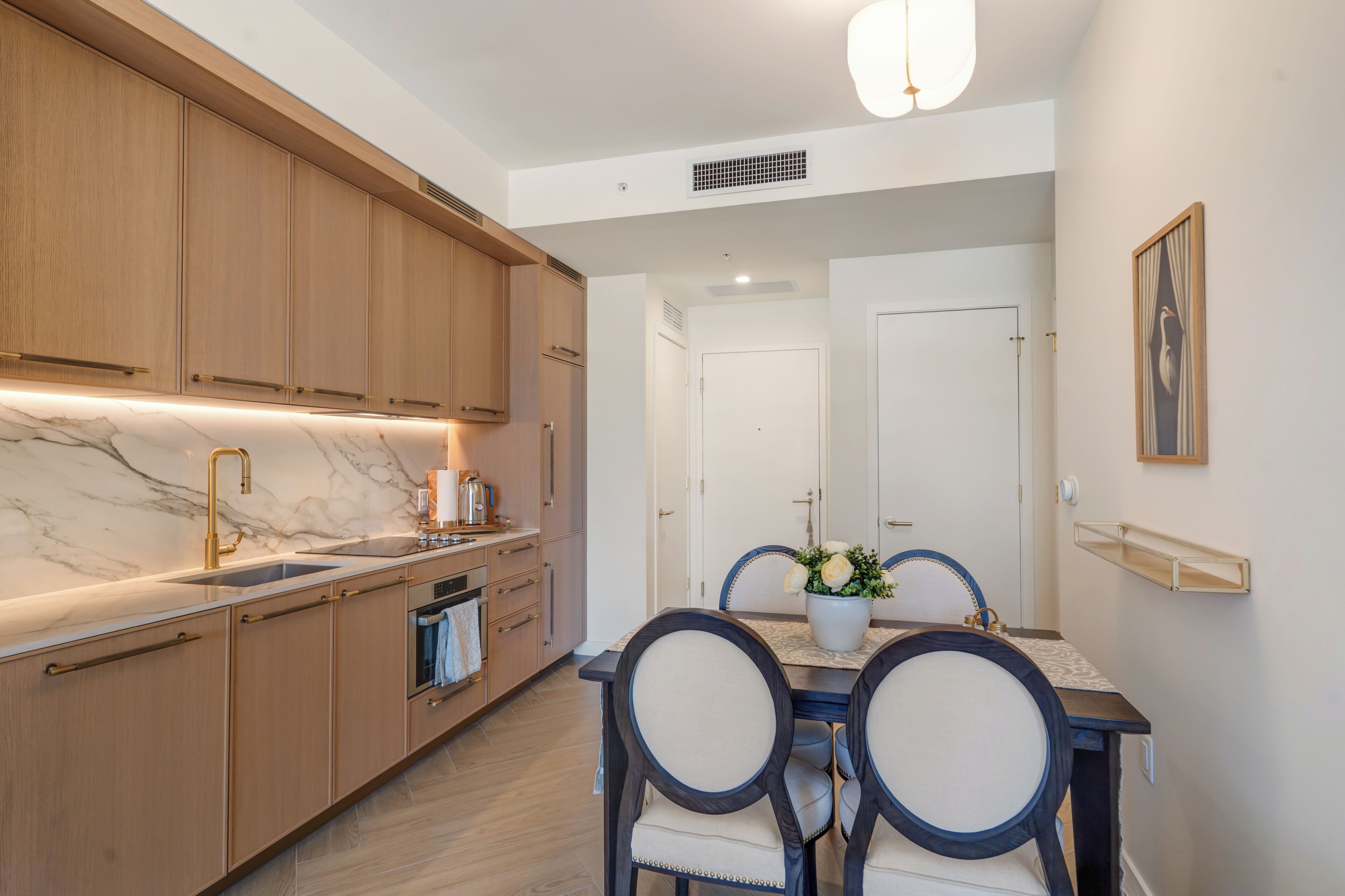 A modern kitchen with wooden cabinets, a marble countertop, and a dining area with a table and chairs.