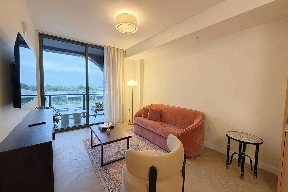 Una sala de estar moderna con un sofá, una mesa de centro, un televisor montado en la pared y un balcón con vistas.