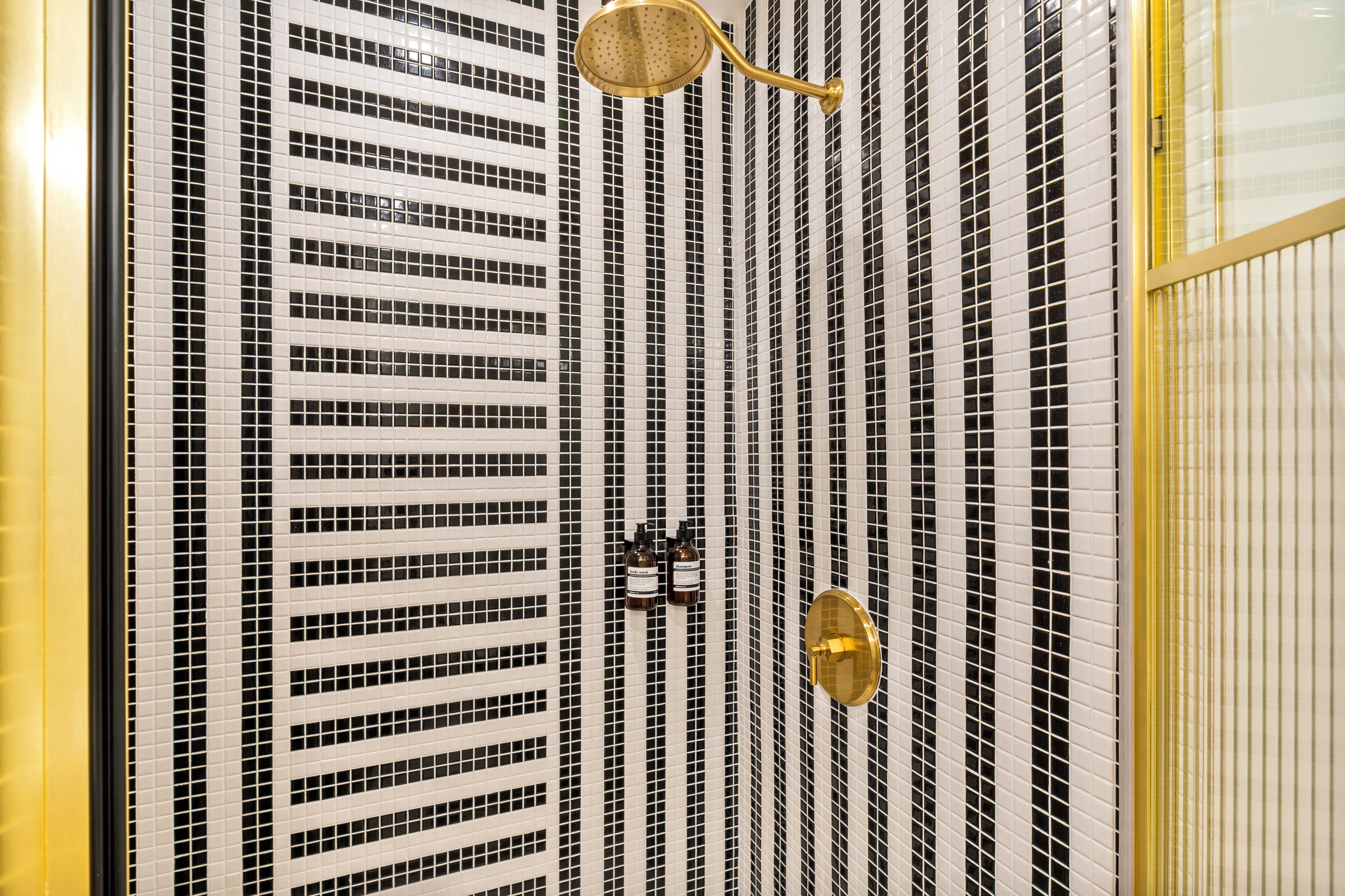 A bathroom with a tiled wall, a gold showerhead, and a gold faucet.