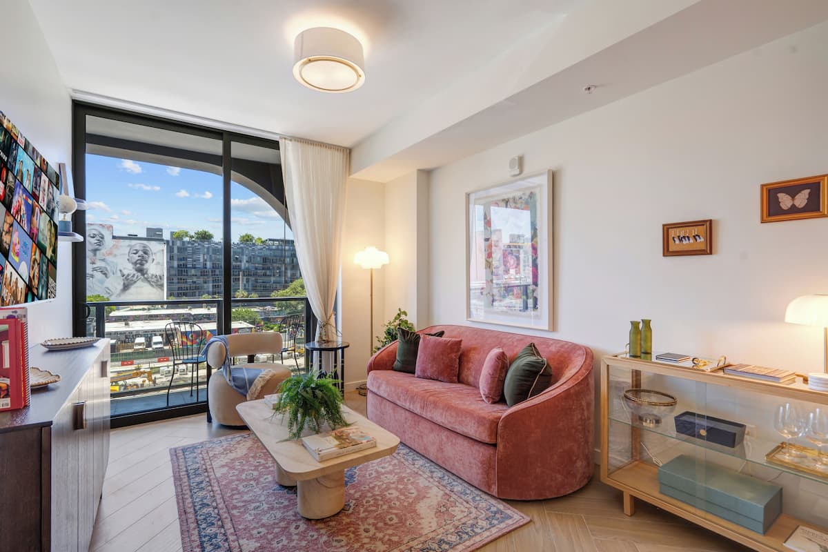 Una sala de estar moderna con un sofá, una mesa de centro y vistas de la ciudad a través de amplios ventanales.