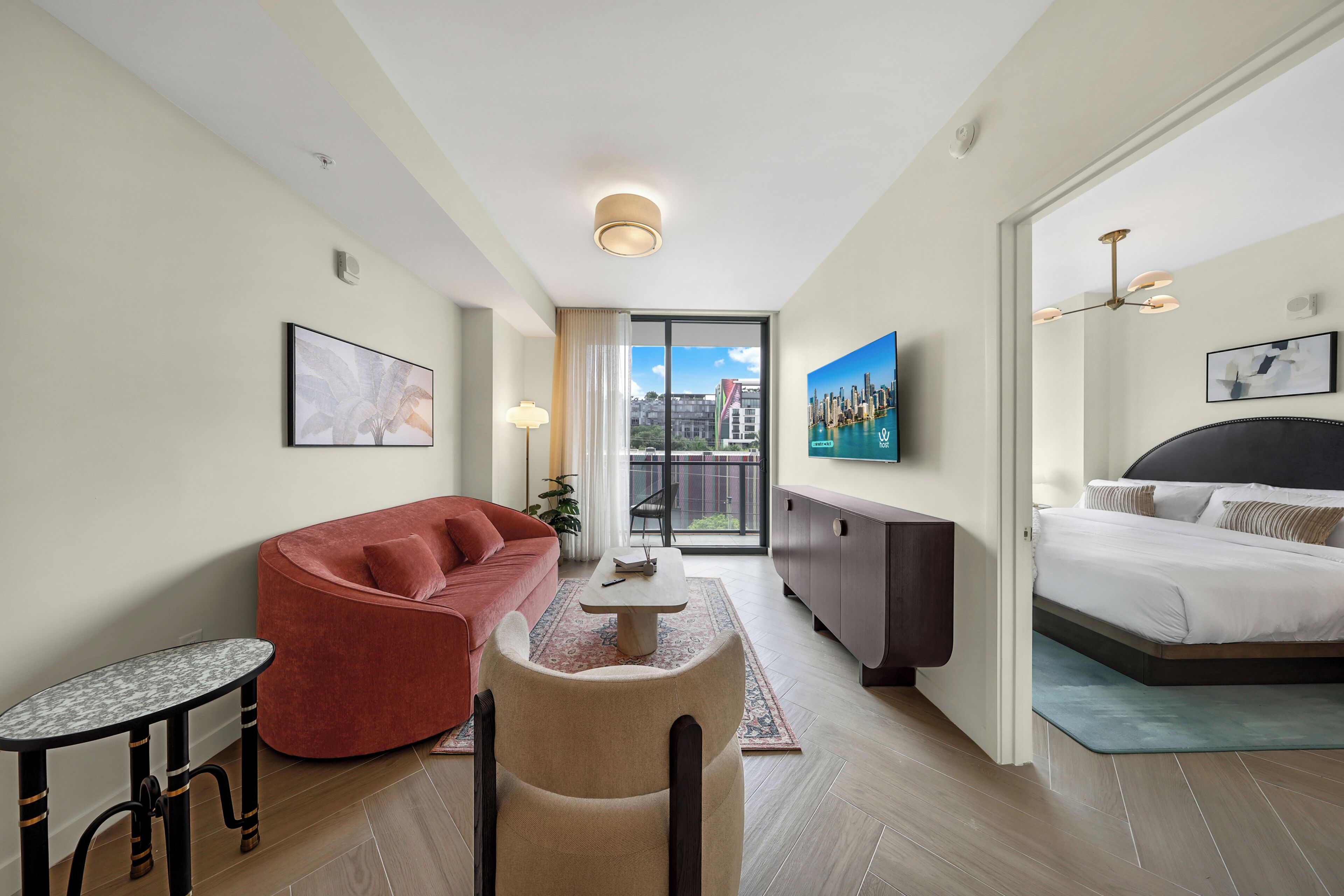 Una habitación de hotel moderna con sofá, una mesita, cama, televisor y balcón con vistas a la ciudad.