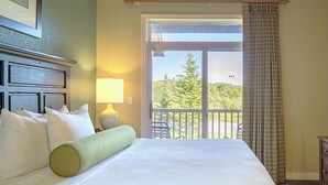 Ein Hotelzimmer mit Bett, Fernseher, Lampe und einem Balkon mit Blick auf Bäume.