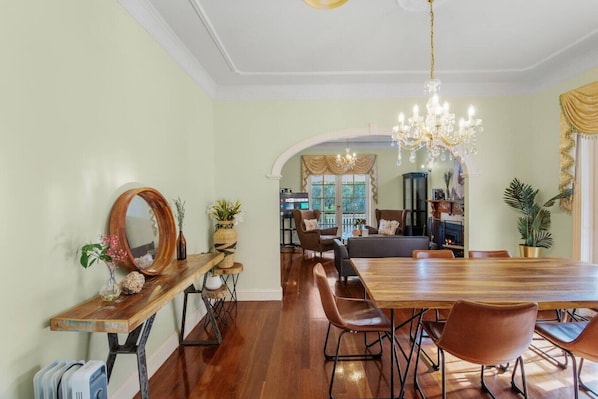 A dining area with a wooden table and chairs, a chandelier, and a view of the living room.