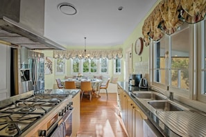 A kitchen with a gas stove, a dining area with a table and chairs, and a window with curtains.