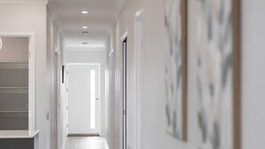 A long, narrow hallway with a light-colored floor and white walls. There are doors on both sides of the hallway, and the walls are adorned with abstract art. - Brand New Family Home | Space, Comfort & Location (Park Ridge)