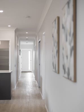 A long, narrow hallway with a light-colored floor and white walls. There are doors on both sides of the hallway, and the walls are adorned with abstract art.