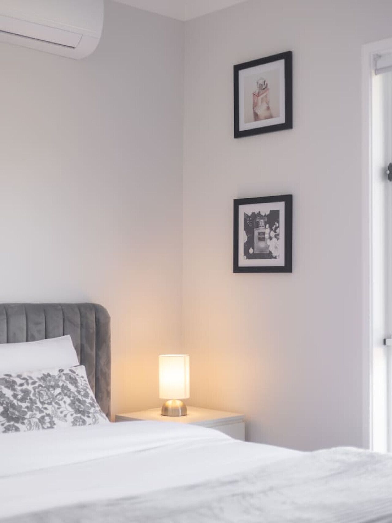 A bedroom with a bed, a bedside lamp, and two framed pictures on the wall.