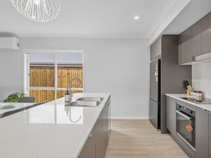 A modern kitchen with a large island, stainless steel appliances, and a view of a wooden fence outside.
