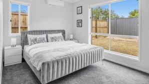 A bedroom with a bed, a nightstand, a ceiling fan, and a large window. - Brand New Family Home | Space, Comfort & Location (Park Ridge)