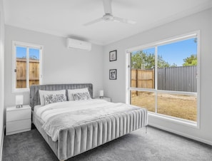 A bedroom with a bed, a nightstand, a ceiling fan, and a large window.