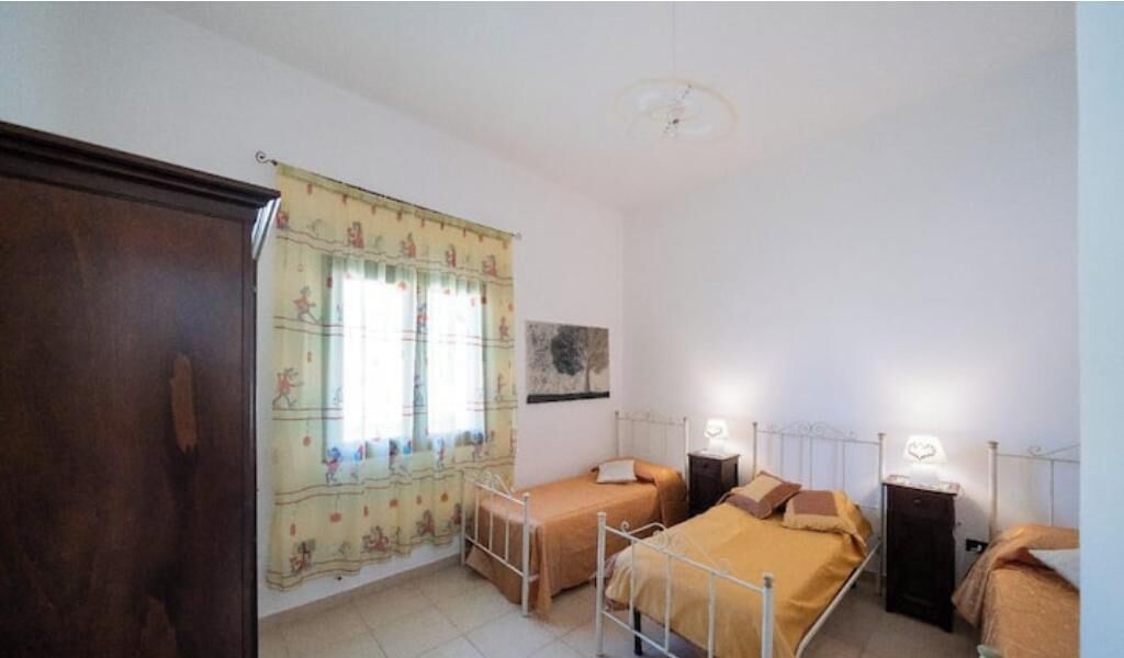 A room with two beds, a wardrobe, a window with curtains, and a wall-mounted picture.
