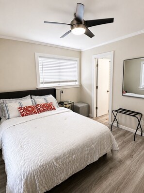 A bedroom with a bed, a ceiling fan, a bedside table, a nightstand, a mirror, and a door. - Condo walking distance to Coligny Beach, Shops & Dining. Your Hilton Head Haven! (Hilton Head Island)
