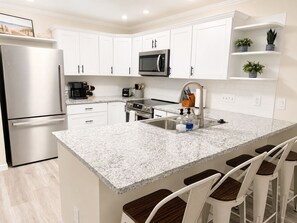 A modern kitchen with white cabinets, a stainless steel refrigerator, a microwave, a coffee maker, and a sink with bar stools. - Condo walking distance to Coligny Beach, Shops & Dining. Your Hilton Head Haven! (Hilton Head Island)