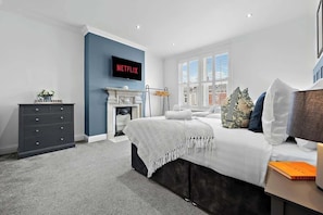 Un dormitorio con cama, cómoda, chimenea, televisor y ventana.