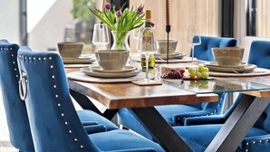 A dining table with blue upholstered chairs, a glass top, and a vase with purple flowers. - Charming Portsmouth Home w/ Private Garden (Portsmouth)
