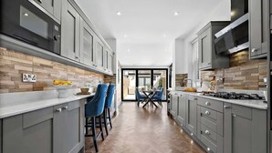 A modern kitchen with grey cabinets, a wooden herringbone floor, and a dining area with blue chairs. - Charming Portsmouth Home w/ Private Garden (Portsmouth)