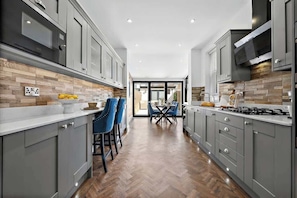 Una cocina moderna con armarios grises, suelo de madera en patrón de espiga y un comedor con sillas azules.