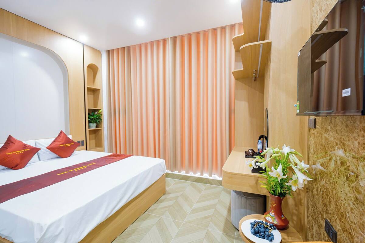 Una habitación de hotel con una cama, un escritorio, un jarrón con flores y vistas a un edificio.