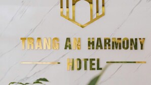 En logotyp med en hexagonformad design och texten ”TRANG AN HARMONY HOTEL” på en vägg av marmor.