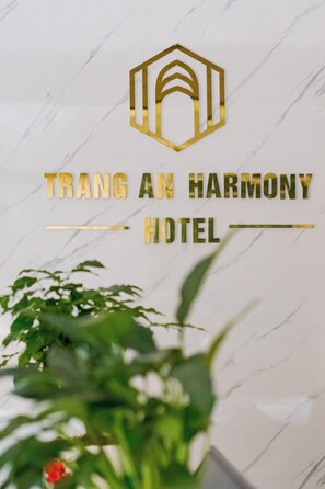 Un logotipo con un diseño hexagonal y el texto 'TRANG AN HARMONY HOTEL' sobre una pared de mármol.