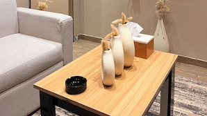 Quarto com televisão de tela plana na parede, uma mesa de madeira com três vasos, um sofá e um aparelho de ar condicionado.